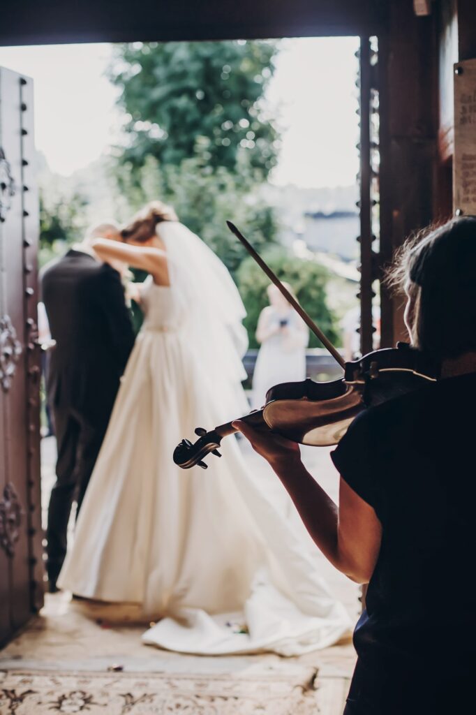 Musician playing on violin while beautiful bride and groom standing in church